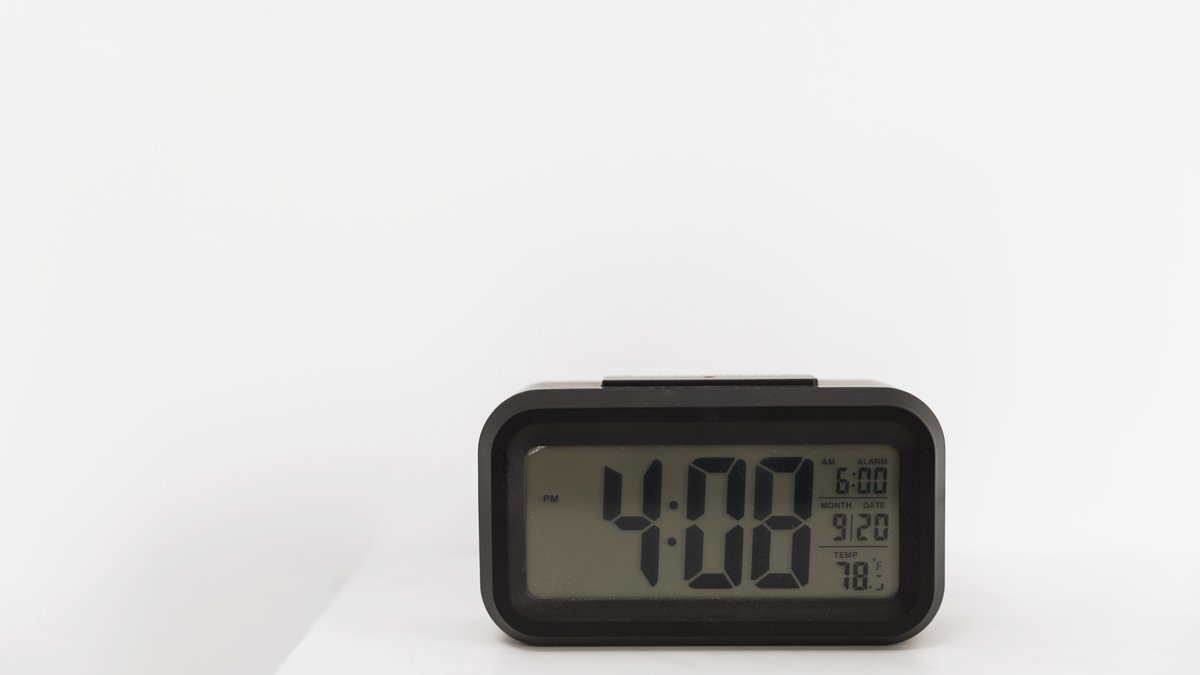 Close-up of a modern bedside digital alarm clock with red LED display being inspected for concealed camera optics
