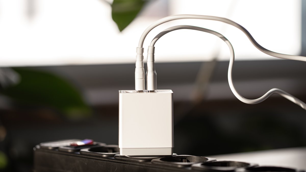 Close-up of white USB wall charger adapter plugged into bedroom socket being inspected for pinhole camera lens