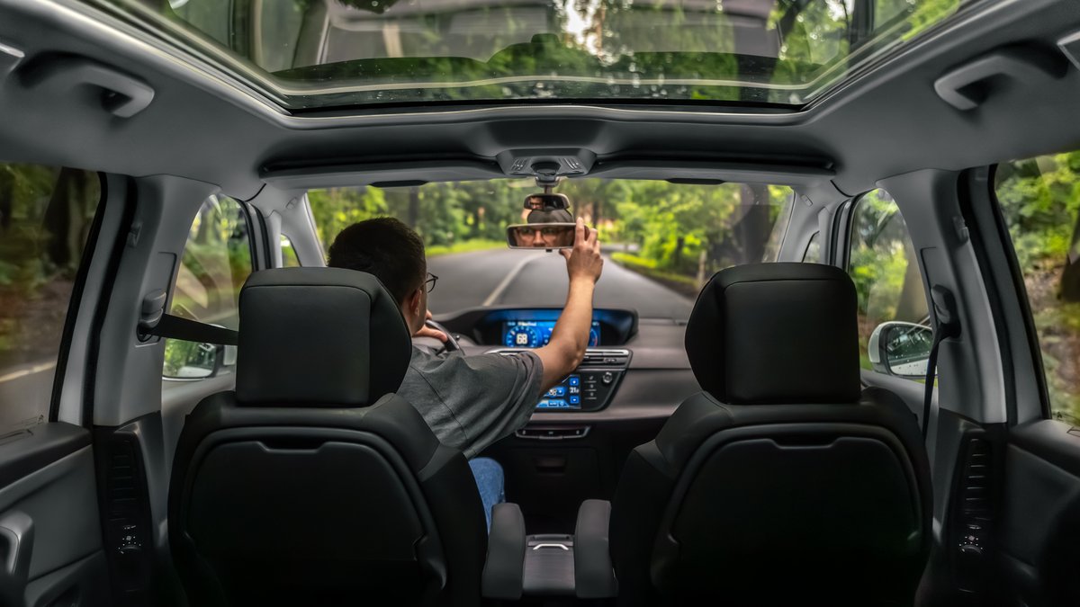 Driver adjusting rearview mirror inside modern automobile cockpit during security inspection