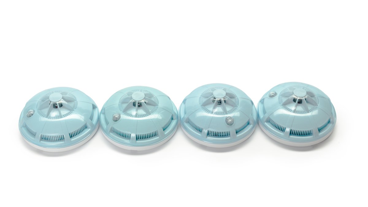 Close-up of a ceiling mounted smoke detector being inspected for hidden camera lenses and decoy hardware